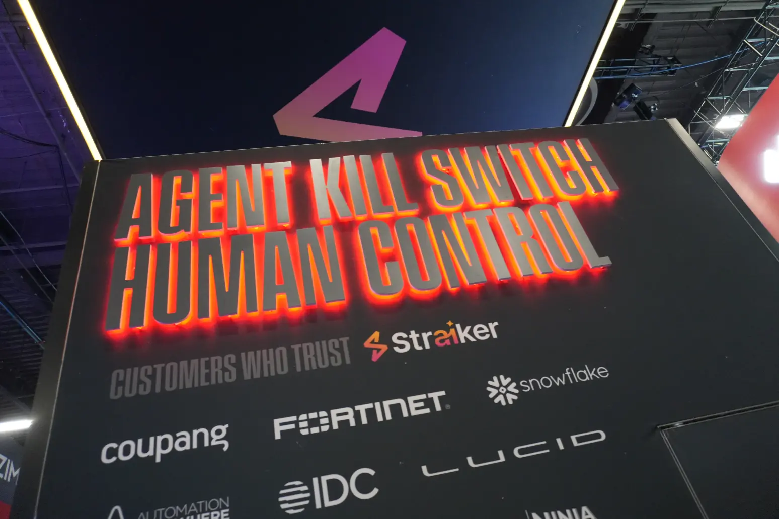 Straiker AI custom backlit backwall branding and exhibit booth design at cybersecurity trade show, featuring bold graphic displays.
